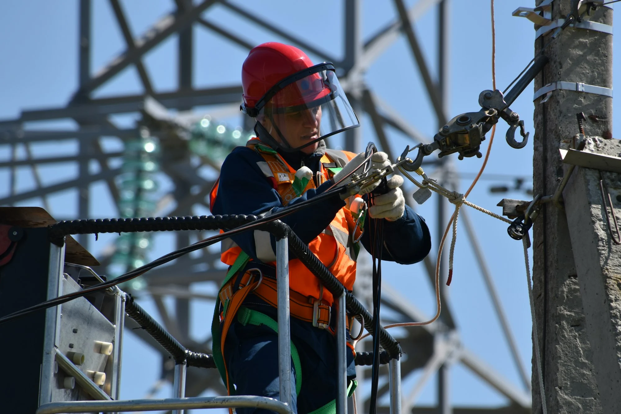 Técnico liniero trabajando en torre de alta tensión con arnés de seguridad