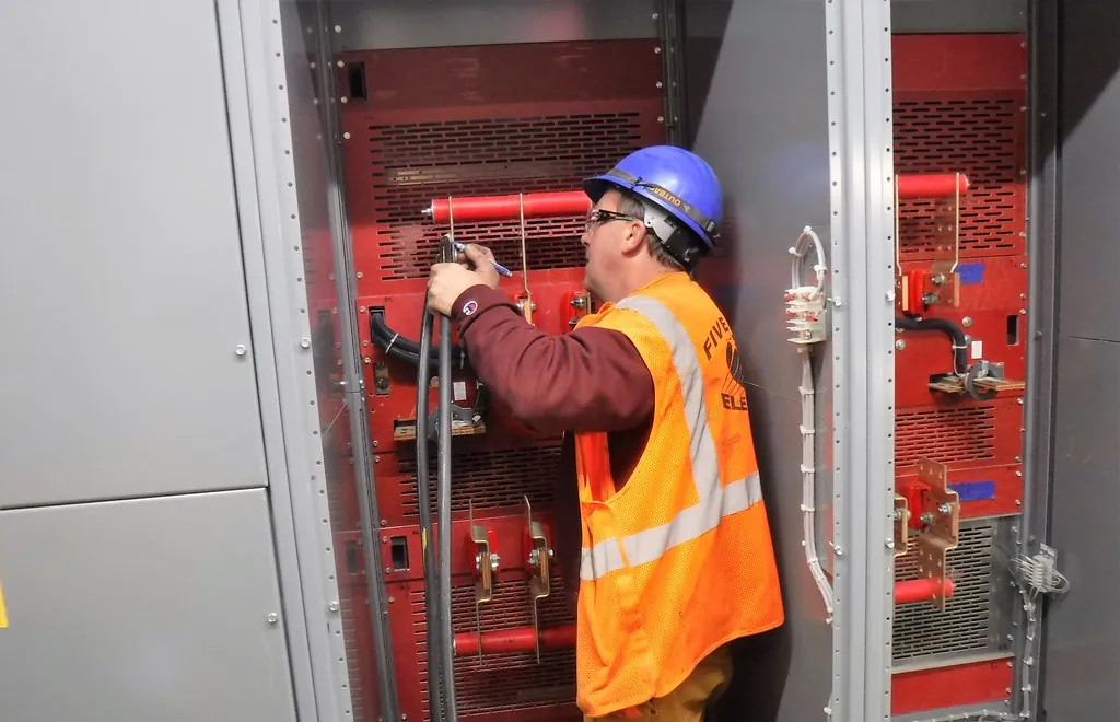 Técnico con casco trabajando dentro de un tablero de distribución en una subestación