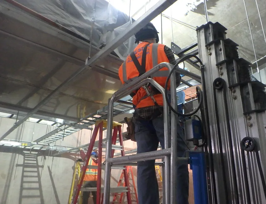 Técnico en una plataforma elevada revisando charolas portacables en el techo de una instalación industrial